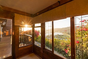 A room with large windows, a wooden floor, and a view of a landscape with flowers.