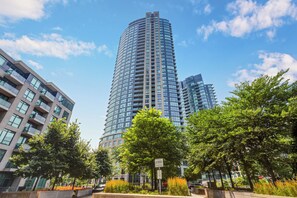 A modern high-rise building with a curved facade, surrounded by trees and other buildings.