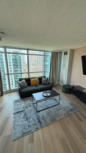 A modern living room with a sofa, a coffee table, and a view of high-rise buildings. - Fort Harbour Suites - Downtown Toronto (Toronto)