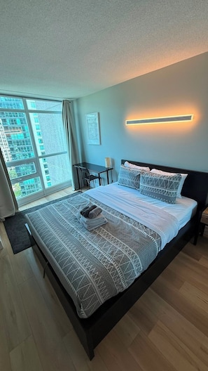 A modern bedroom with a large bed, a desk, and a window with a city view. - Fort Harbour Suites - Downtown Toronto (Toronto)
