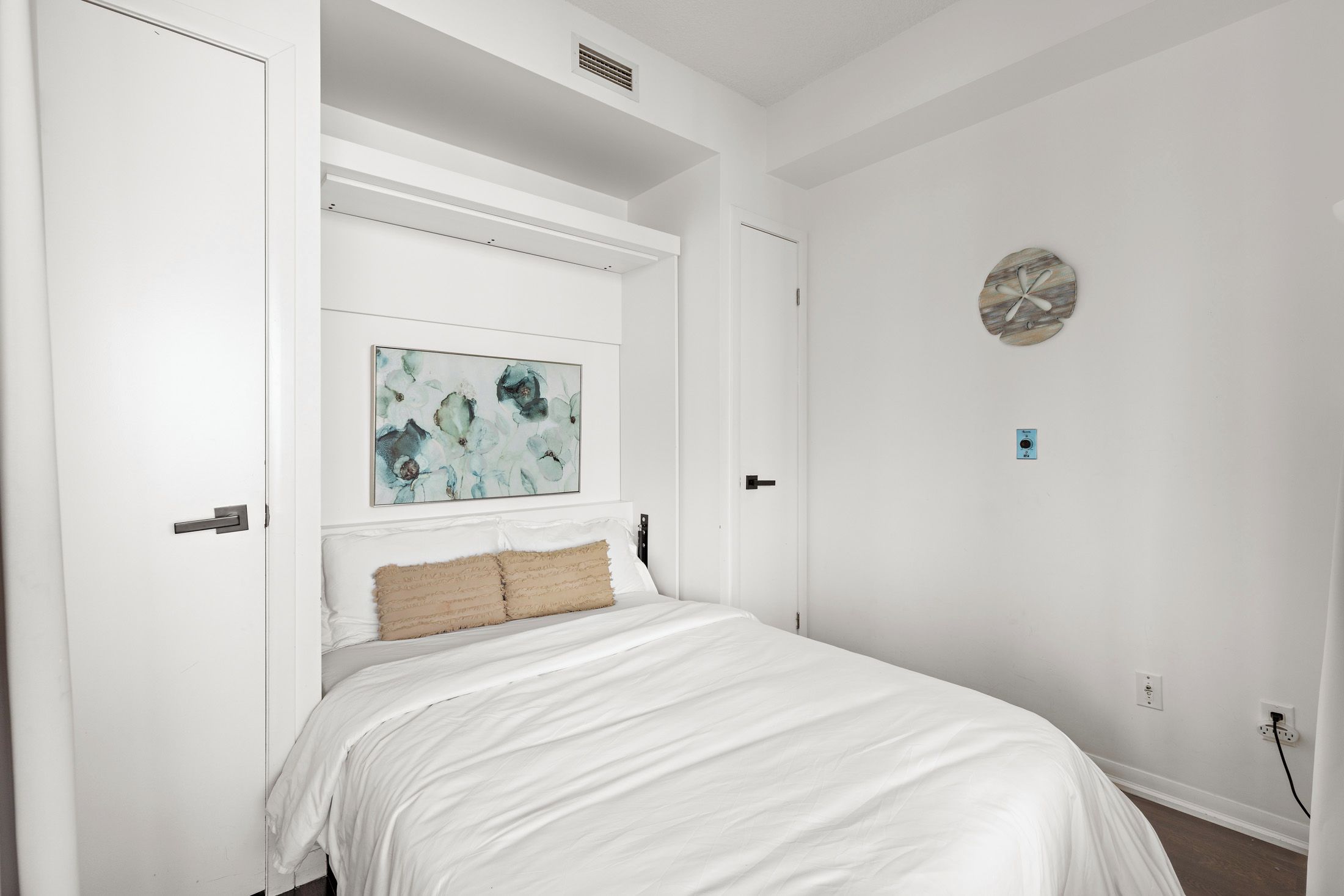A bedroom with a bed, a painting, a wall clock, and a door.