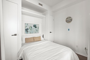 A bedroom with a bed, a painting, a wall clock, and a door.