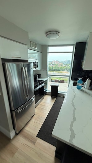 A modern kitchen with a stainless steel refrigerator, oven, and microwave. There is a large window providing a view of the cityscape. - Fort Harbour Suites - Downtown Toronto (Toronto)