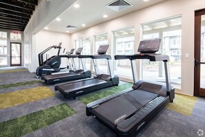 Academia com esteiras, bicicletas ergométricas e piso coberto de carpete.