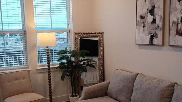 A living room with a sofa, armchair, floor lamp, and a large mirror. - Resort-Style Stay | Pool, Gym | Near Toyota Field (Madison)