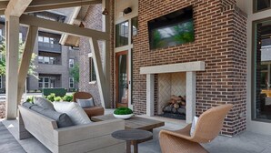 An outdoor seating area with a sofa, chairs, and a table, a fireplace, and a TV mounted on the wall. - Resort-Style Stay | Pool, Gym | Near Toyota Field (Madison)