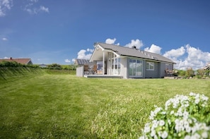 A modern house with a large glass door, a covered patio, and a well-maintained lawn. - Deichperle Vacation Home: No security deposit, no final cleaning fee, no energy costs (Wesselburenerkoog)