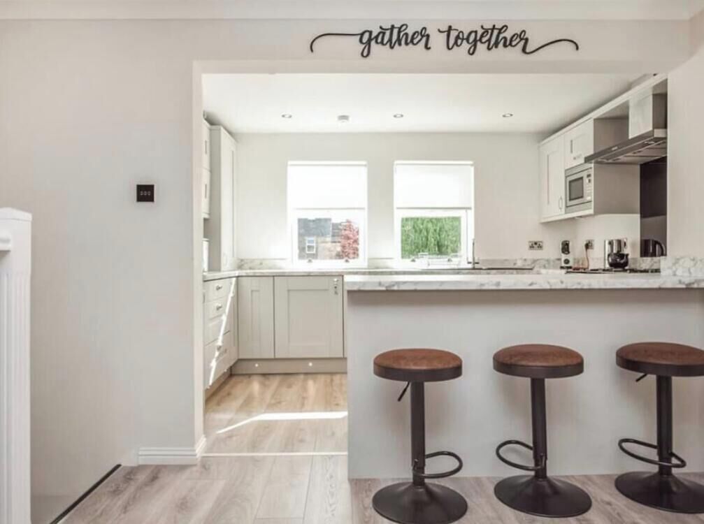 A modern kitchen with white cabinets, a marble countertop, and three stools.