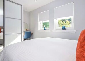 Ein Schlafzimmer mit einem Bett, einem Schreibtisch und zwei Fenstern mit Jalousien.