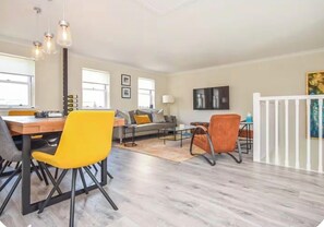 Uma sala de estar moderna com área de jantar, sofá, mesa de centro e televisão na parede.