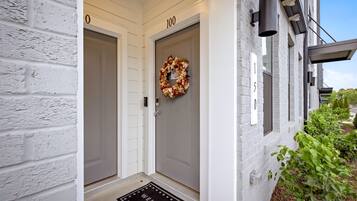 A white building with two doors, each marked with a number, a welcome mat, and a wreath on the door.
