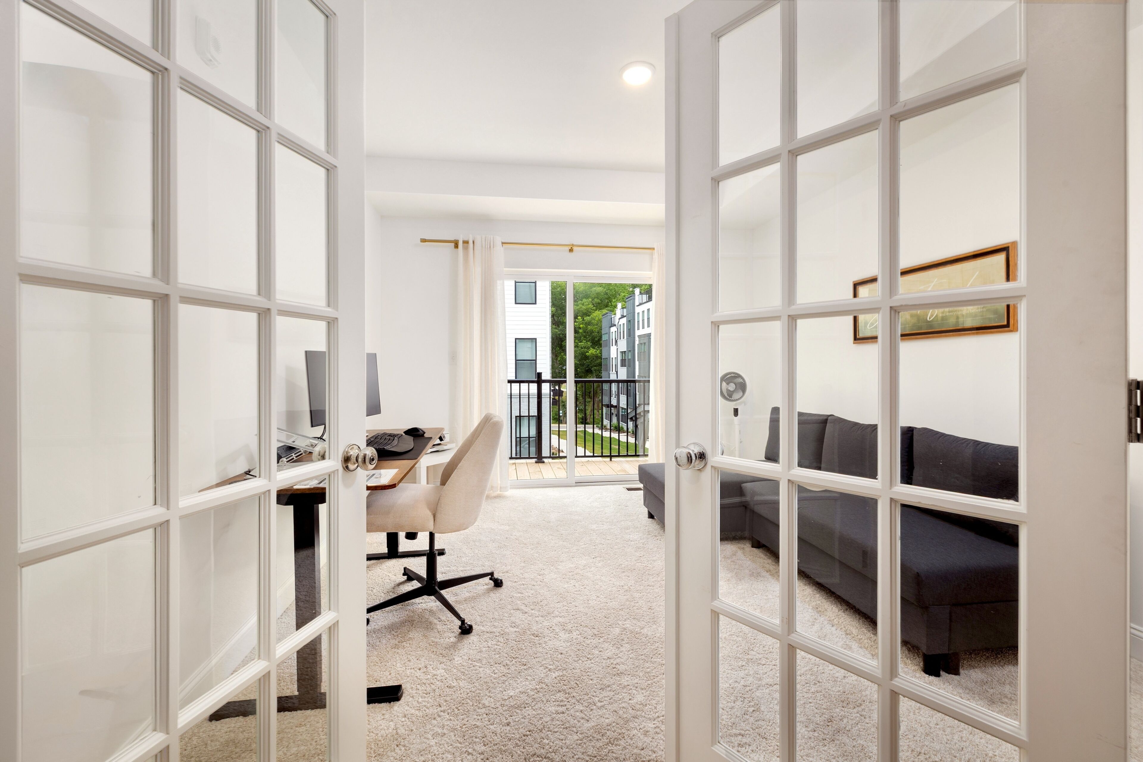 Une pièce comprenant un bureau, une chaise et un canapé, avec vue sur les bâtiments environnants.