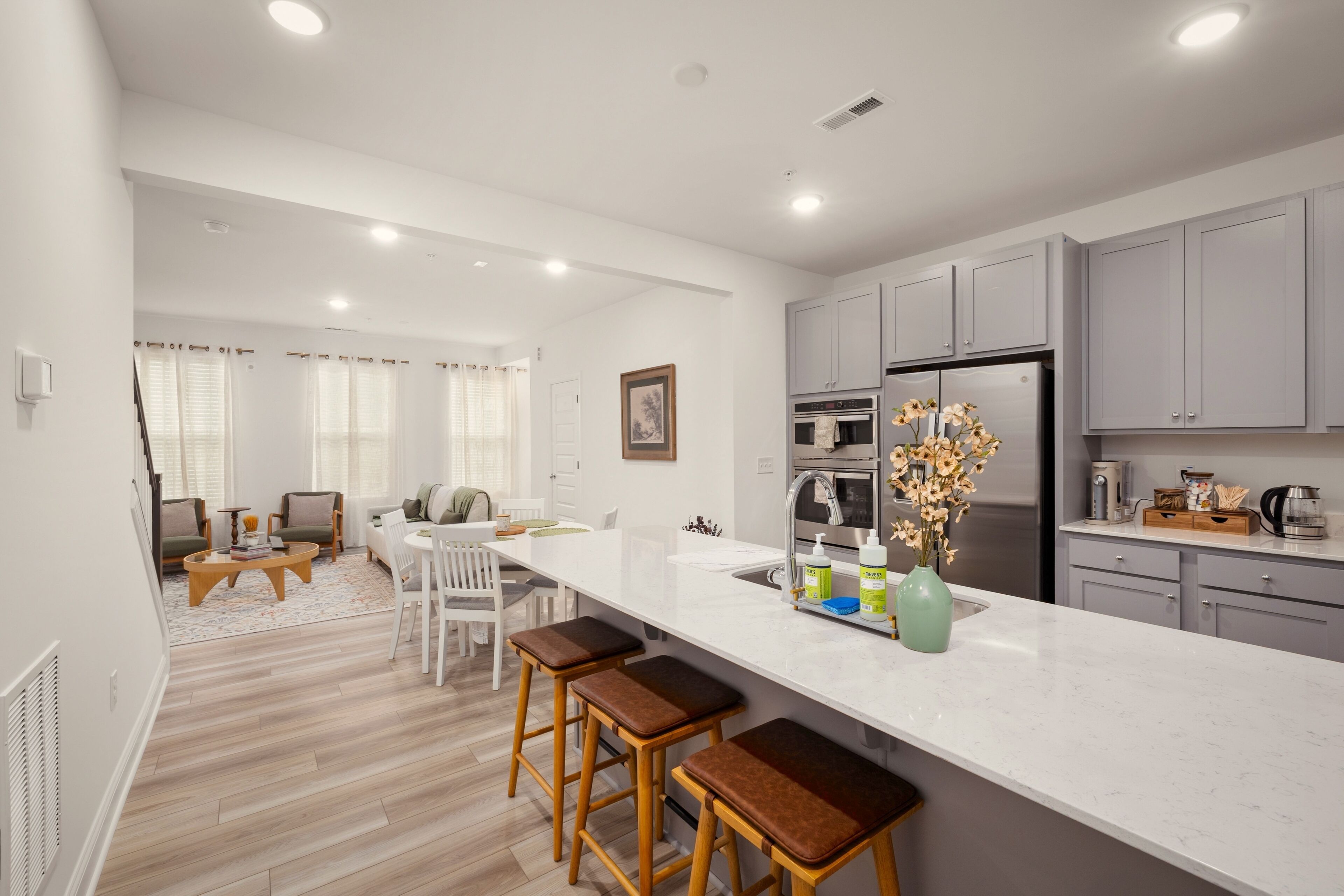A modern kitchen with a white countertop, grey cabinets, and a stainless steel refrigerator.