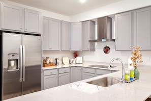 A modern kitchen with grey cabinets, a stainless steel refrigerator, a built-in oven, a sink with a modern faucet, and a coffee maker.
