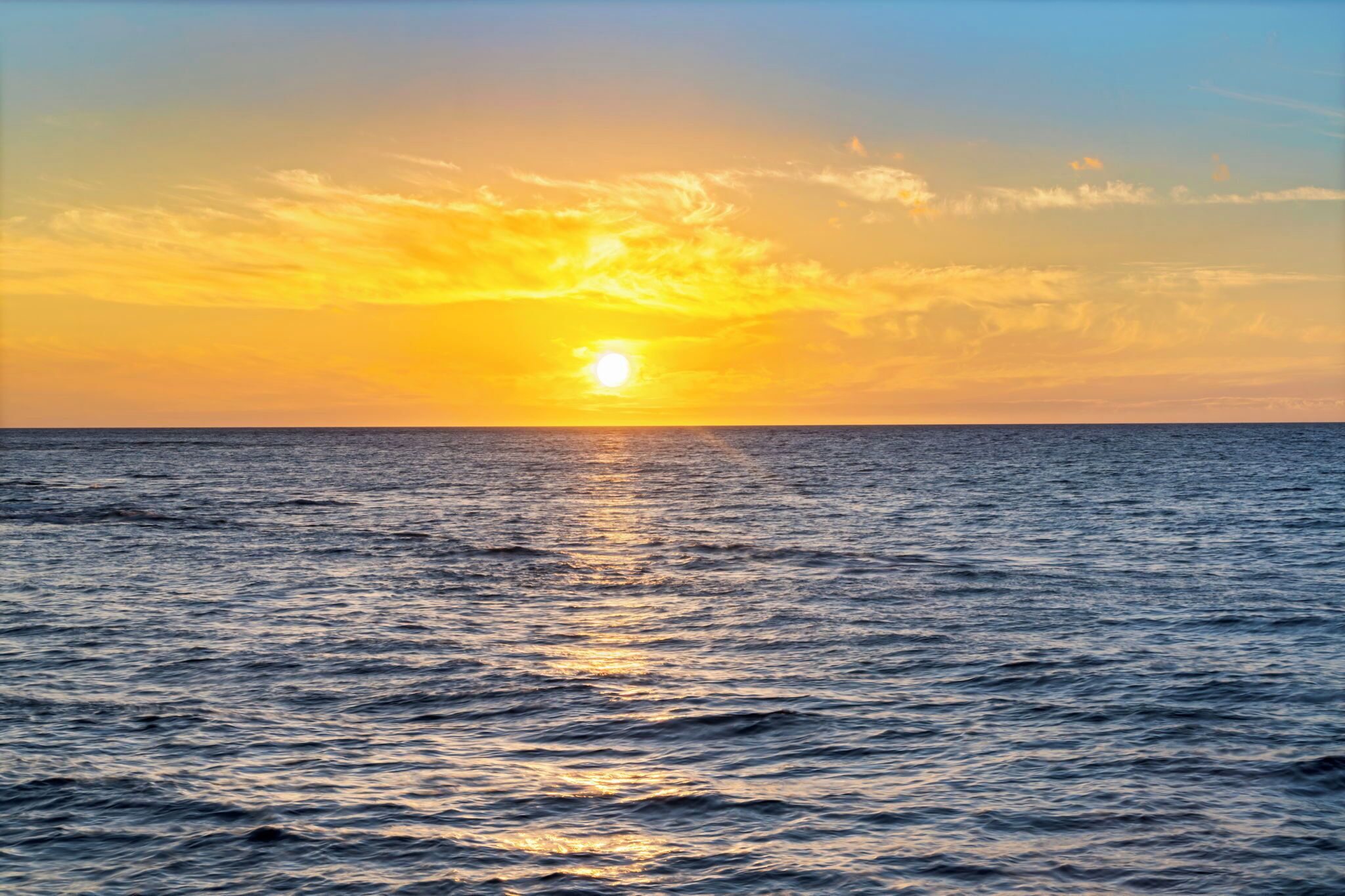 A sunset over the ocean with calm waters reflecting the sky.