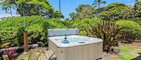 A hot tub in a garden with lush greenery and a clear sky.