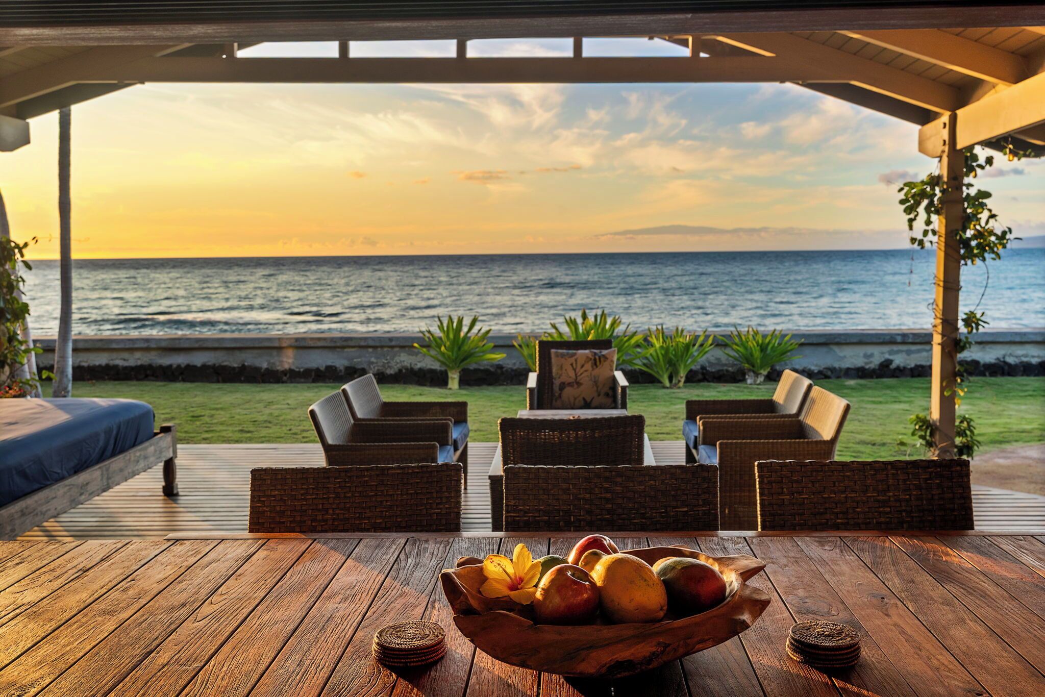 An outdoor seating area with wicker furniture and a wooden deck overlooking the ocean.