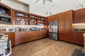 A modern kitchen with wooden cabinets, stainless steel appliances, and a granite countertop. - Island Time Retreat by Gather: Oceanfront Access (Kamuela)