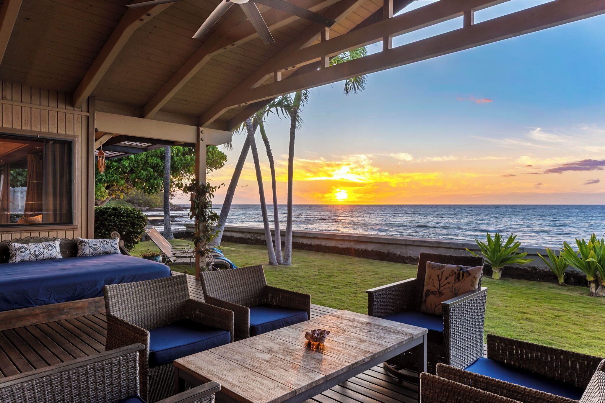 A covered outdoor seating area with a view of the ocean at sunset.