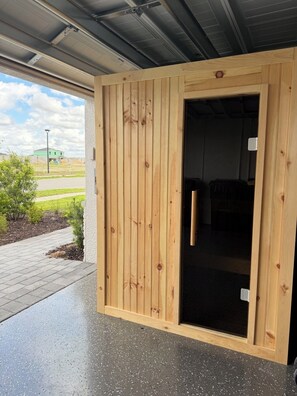 A wooden door leading to a room with a dark floor, a visible light switch, and a view of a green building in the background. - Gated Babcock Ranch Home - Pool, Spa, Sauna & Lake View (Punta Gorda)