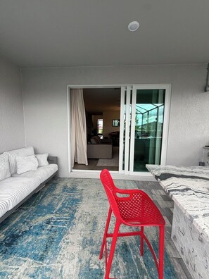 A room with a sofa, a red chair, a patterned rug, and a sliding glass door leading to another room. - Gated Babcock Ranch Home - Pool, Spa, Sauna & Lake View (Punta Gorda)