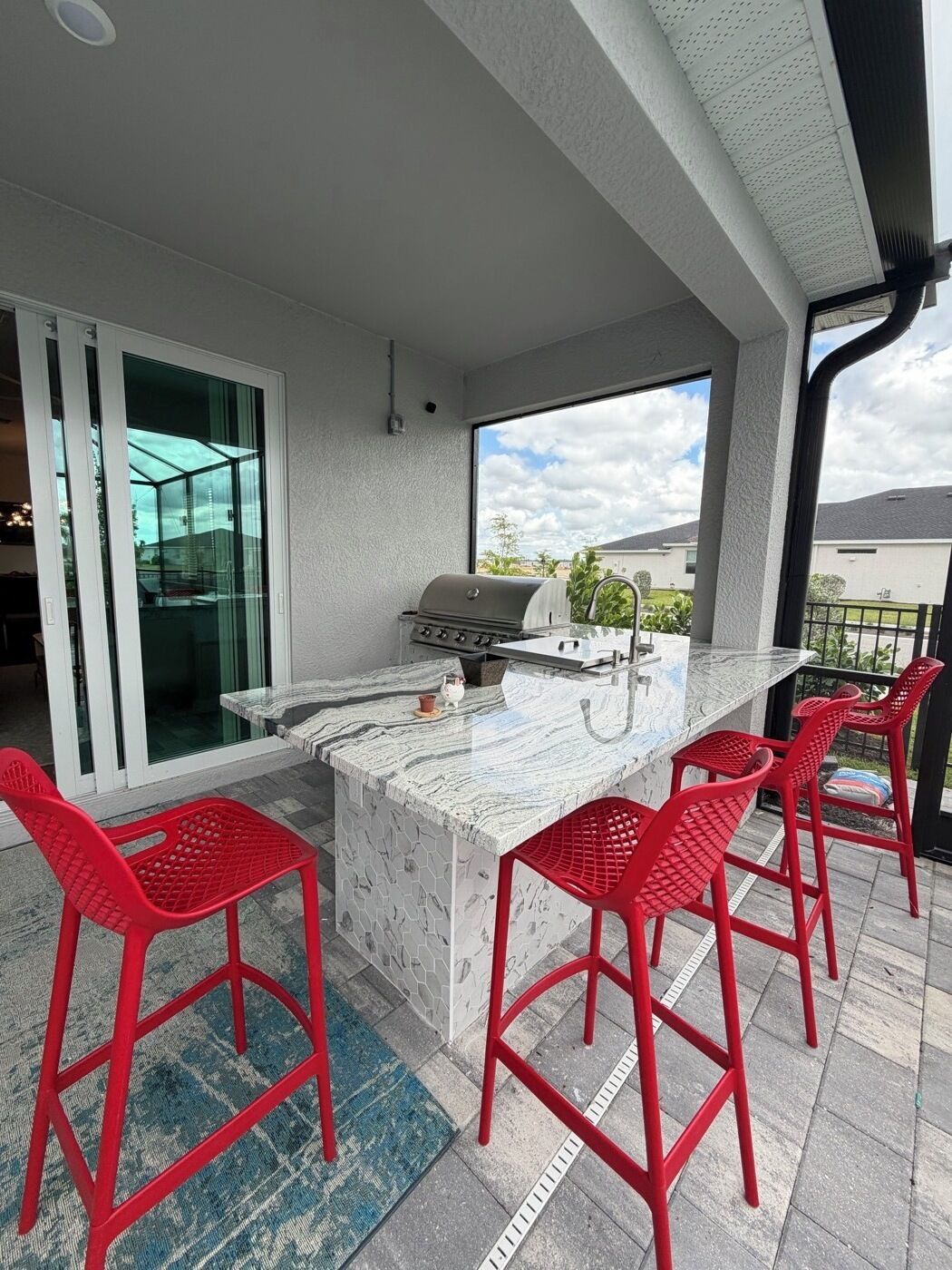 An outdoor kitchen area with a grill, bar stools, and a view of the neighborhood.