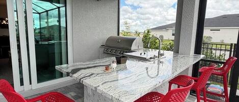An outdoor kitchen area with a grill, bar stools, and a view of the neighborhood.