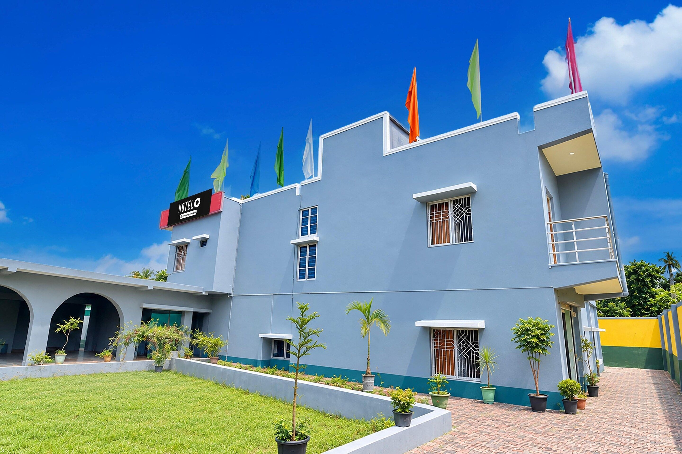 A hotel with a modern facade, multiple windows, and a sign indicating it's a hotel. There are potted plants and a well-maintained lawn in front.