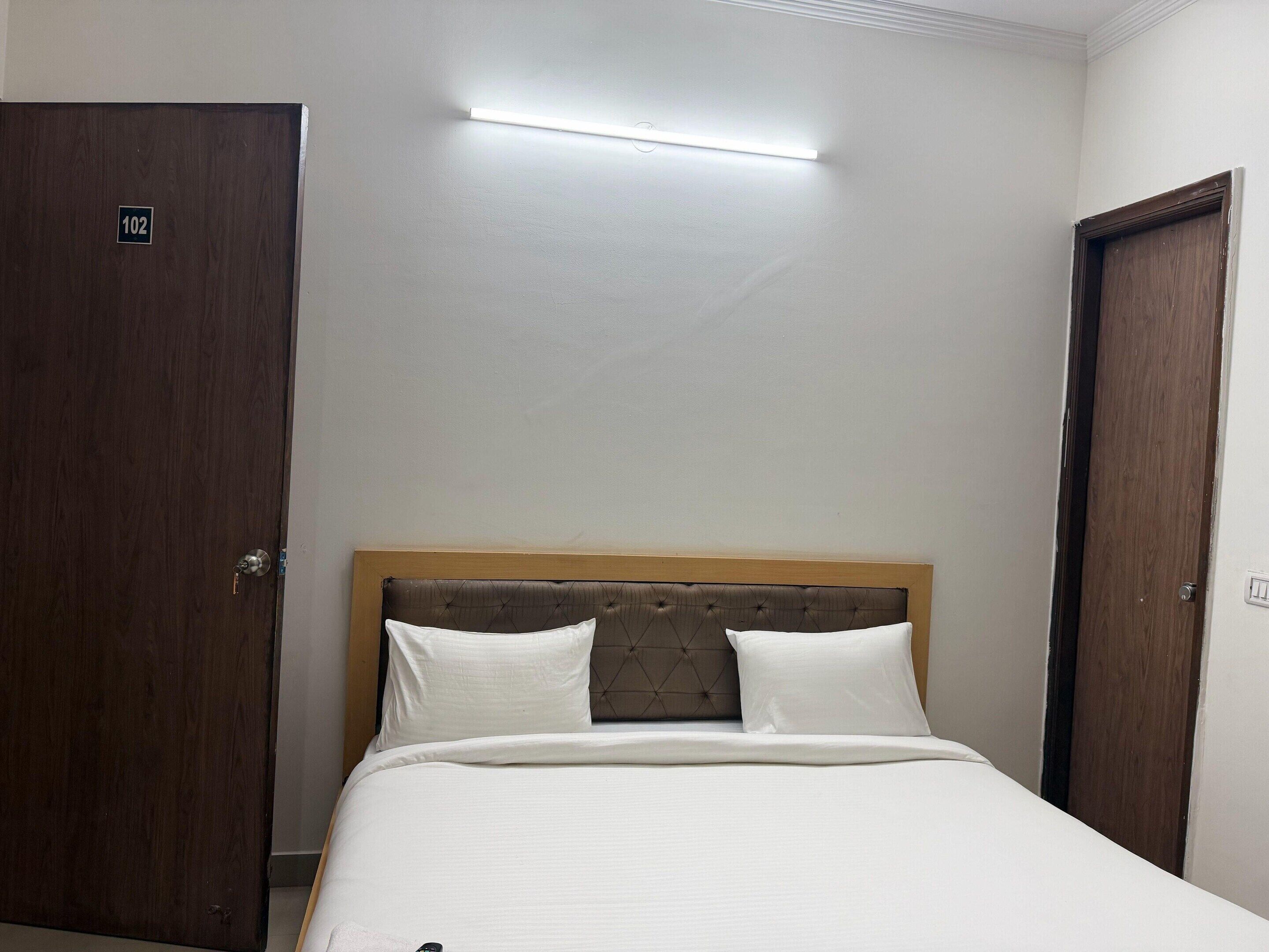 A hotel room with a bed, a wooden door, and a light fixture.