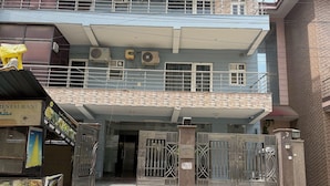A building with a gated entrance, multiple air conditioning units, and a signboard with a phone number.