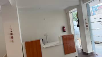 A reception desk with a white wall, a fire extinguisher mounted on the wall, and a door leading outside.