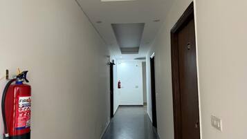 A corridor with a fire extinguisher mounted on the wall, a door on the right, and a ceiling with recessed lighting.