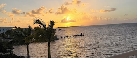 Un balcón con barandilla que da a una masa de agua al atardecer.