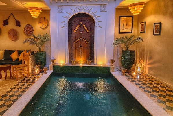 A pool area with a checkered floor, a wooden door with decorative carvings, and wall-mounted lights. - Vrbo Property (Marrakech)