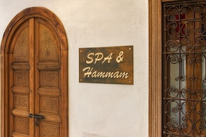 Una porta de fusta amb detalls escultòrics complexos, un rètol que diu 'SPA & Hammam', i una reixa de ferro forjat.