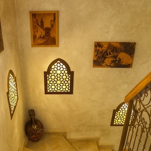 Una escala amb barana de metall ornamentada, un ampolla decoratiu i detalls decoratius a la paret.