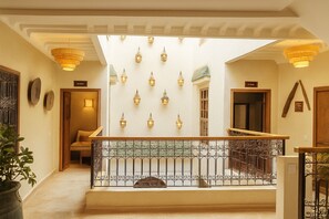 A spacious interior with a high ceiling, a staircase with a wrought iron railing, and multiple wall-mounted light fixtures. - Ourika, Riad Belikoss Pool and Spa (Marrakech)