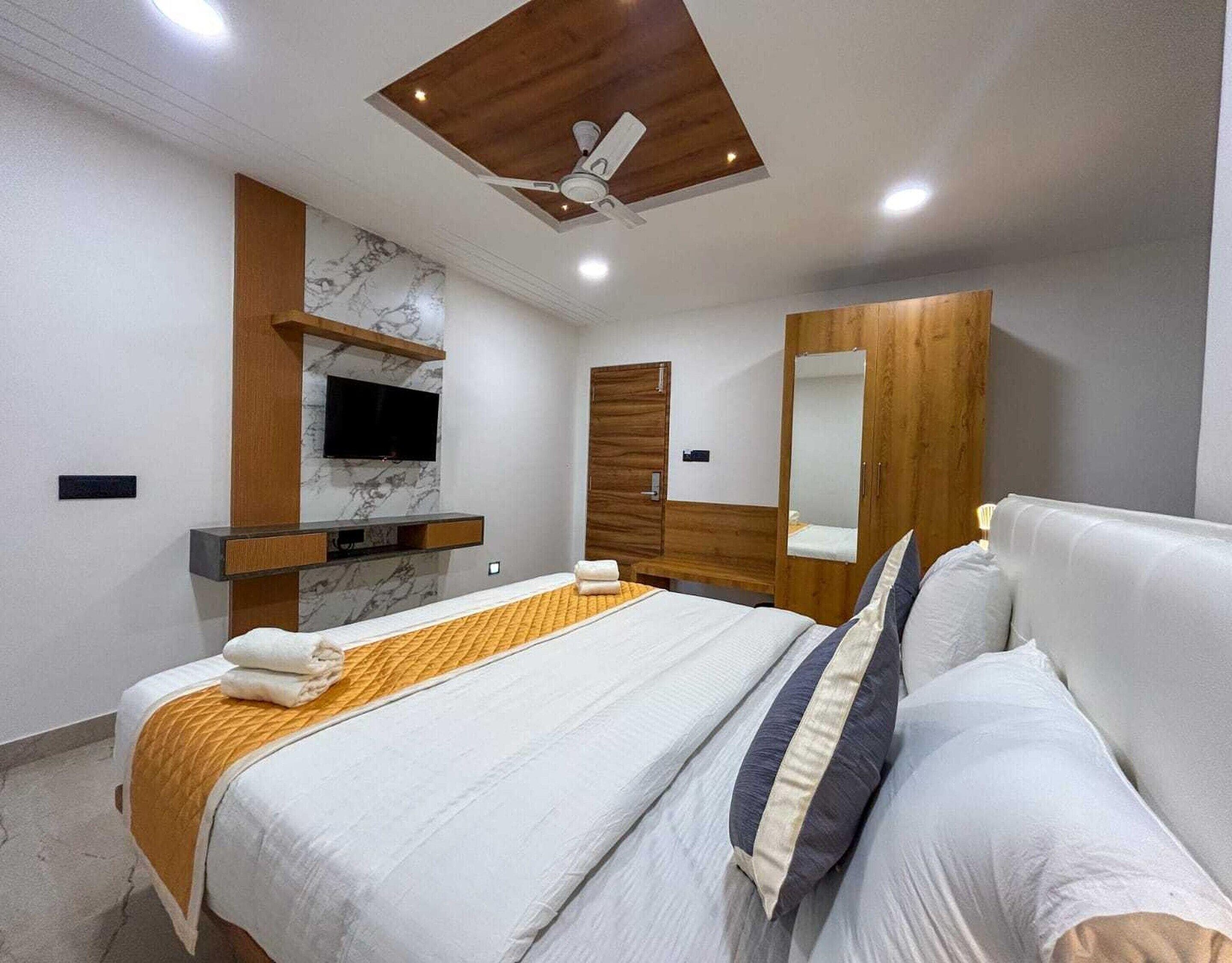 Quarto moderno com cama, televisão, guarda-roupa e ventoinha no teto.