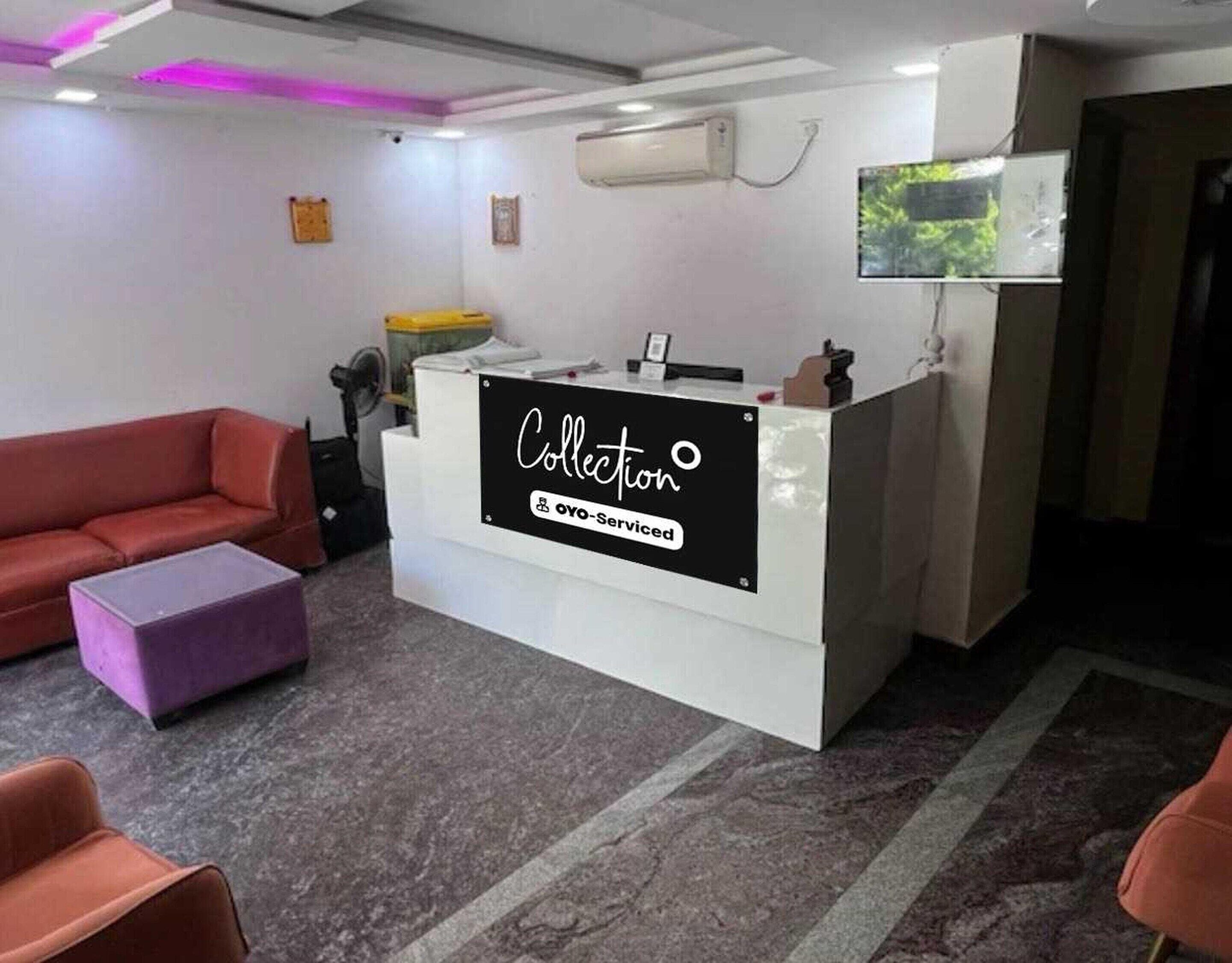 A reception area with a reception desk labeled 'Collection OYO-Serviced,' a red sofa, a purple ottoman, and a television mounted on the wall.