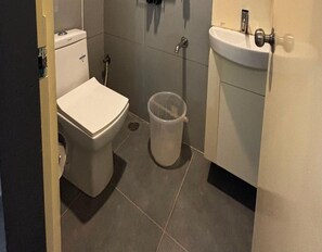 A small bathroom with a toilet, a sink, and a trash bin. - Deluxe Brigade Inn (Bengaluru)