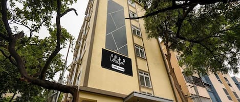 A multi-story building with a beige facade, a large vertical sign with geometric patterns, and a sign indicating 'Collection' and 'OYO-Serviced' services.