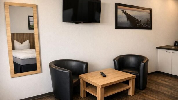 A hotel room with a bed, a TV, a painting, two chairs, and a small table.