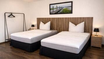 Een hotelkamer met twee bedden, een houten hoofdbord, een ingelijst schilderij aan de muur en een nachtkastje met een lamp.
