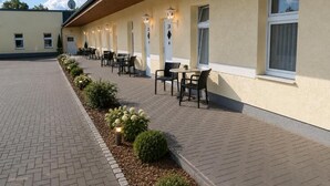 A hotel corridor with outdoor seating, a brick pathway, and a row of windows with numbers.
