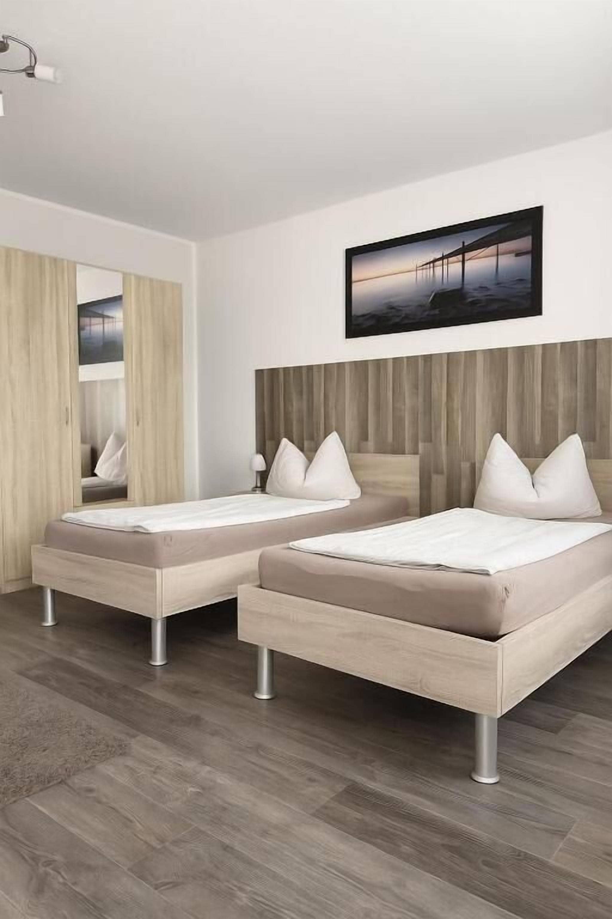 A modern bedroom with two single beds, a wooden headboard, and a large mirror.