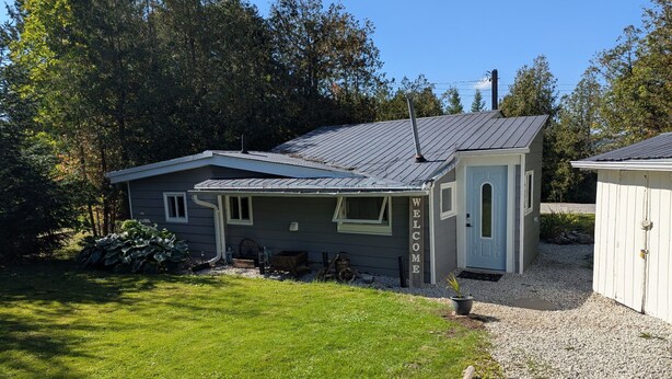 A small, single-story building with a sloped roof, a front porch, and a gravel driveway.