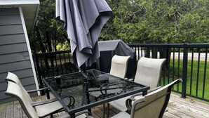 Une terrasse extérieure avec une table et des chaises en verre, un parasol et une plateforme en bois.