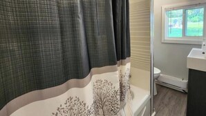 Une salle de bain avec un rideau de douche, des toilettes et une fenêtre.