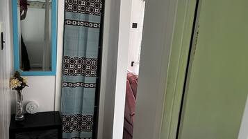 Kapea käytävä, jossa on peili, kuviollinen verho ja pieni pöytä, jonka päällä on maljakko.