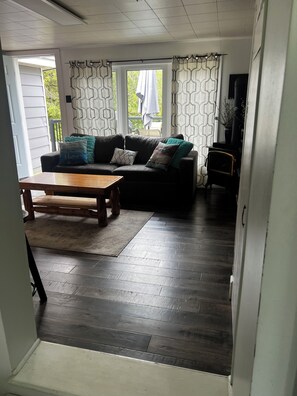 A living room with a dark wood floor, a black sofa with patterned cushions, a wooden coffee table, and a television on a stand.
